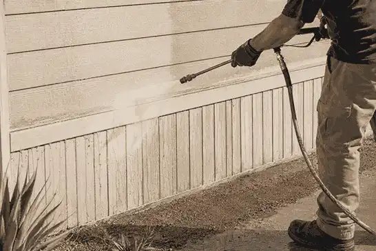A professional worker is power washing the exterior siding of a residential home with a cleaning wand.